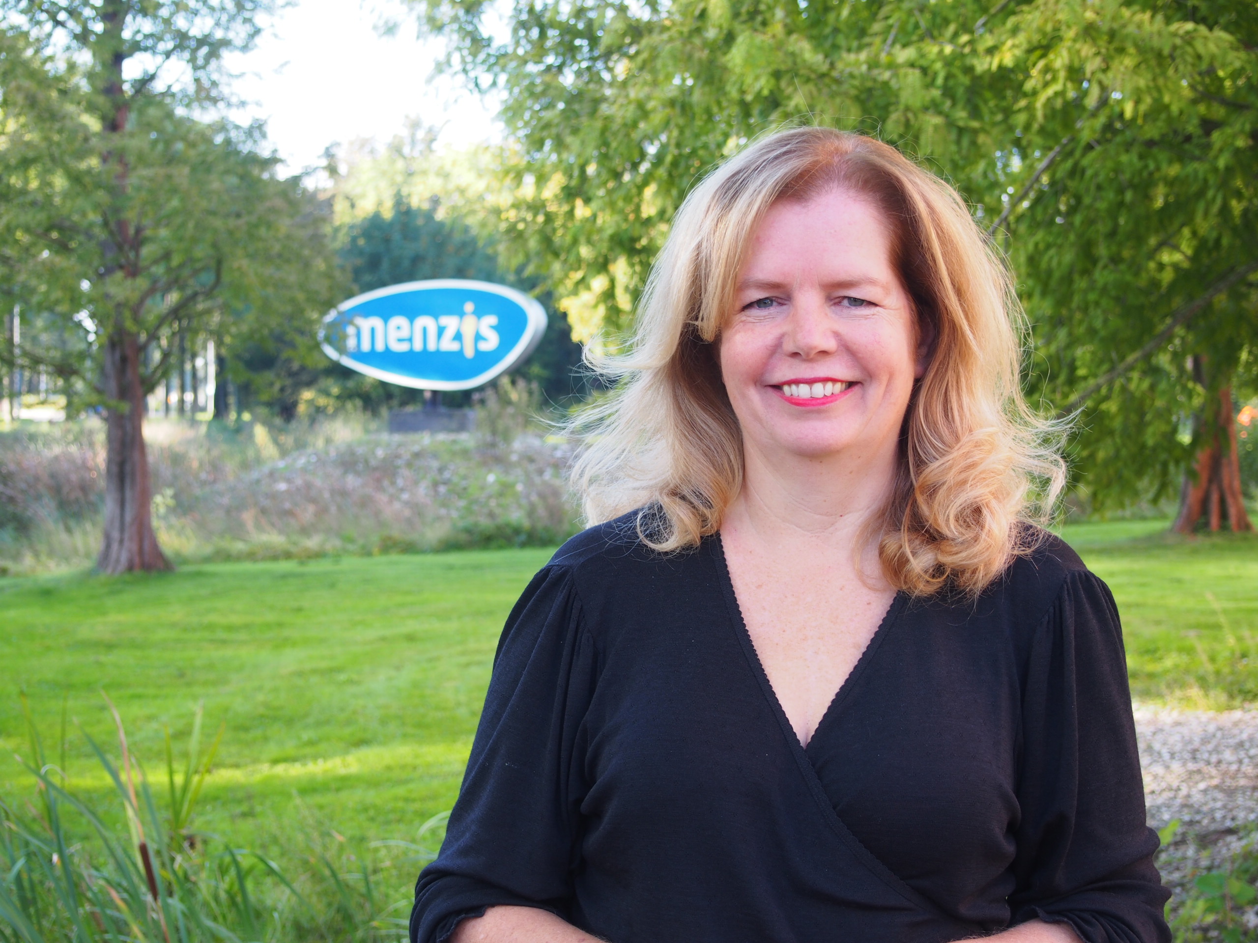 vrouw staat buiten met de achtergrond het logo van Menzis